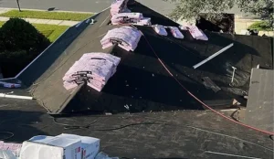 Aerial view of a house roof with visible roof replacement materials like shingles, underlayment, and tools placed on the surface.