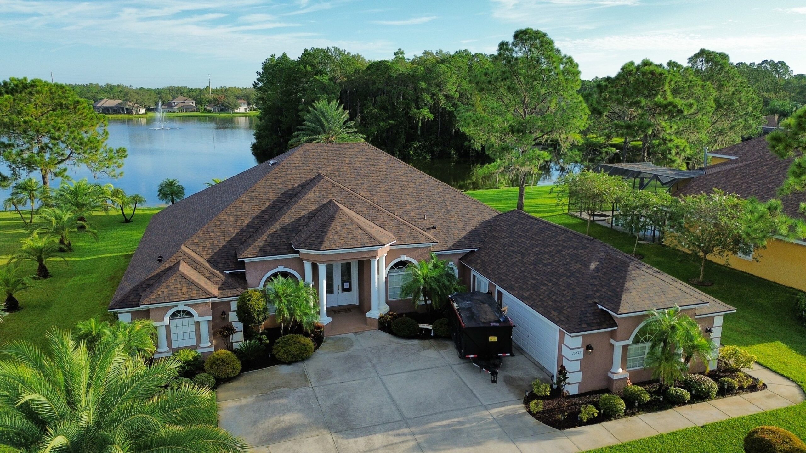 Aerial view from the back of a residential house overlooking a beautiful lake, with landscaped backyard and roofing by JAC Builders